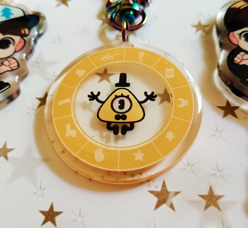 May include: Yellow triangle-shaped character with one eye and a bow tie, inside a clear round keychain with a yellow circle and symbols around the edge.