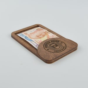 Op de afbeelding: Een houten geldclip met een gleuf voor biljetten en een rond ontwerp met de tekst "Coffee Shop" en een koffiekopje-icoon. De tekst "Premium Quality" is ook in het ontwerp opgenomen.