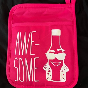 May include: A hot pink oven mitt with the word "AWESOME" in white block letters. A cartoon bottle wearing sunglasses and a Hawaiian shirt is printed on the mitt. The mitt has a pocket and a loop for hanging.
