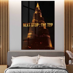 May include: A digital art print featuring a tall, illuminated skyscraper with the text "NEXT STOP: THE TOP" in gold lettering against a dark background.
