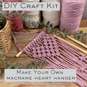 May include: DIY craft kit to make your own macrame heart hanger. The kit includes pink macrame cord, wooden dowel, and instructions. "Make Your Own Macrame Heart Hanger" text is on the image.