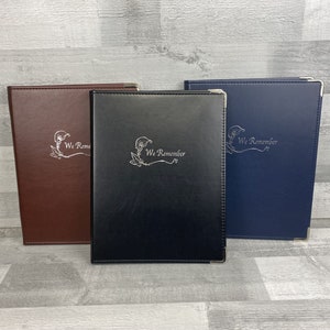 May include: Three folders in different colours, each with a silver trim and the words "We Remember" embossed on the front.