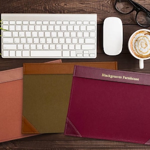May include: Three rectangular desk pads in shades of red, olive green, and brown, with a leather-like top and corner accents. The burgundy pad has "Blackgreaves Farmhouse" printed on it. A keyboard, mouse, coffee, and notepad are also visible.