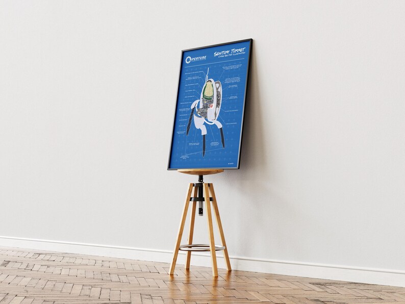 May include: A framed blueprint-style poster featuring a detailed diagram of a "Sentry Turret" from the video game Portal. The poster is displayed on a wooden and metal adjustable stool against a white wall and wooden floor.
