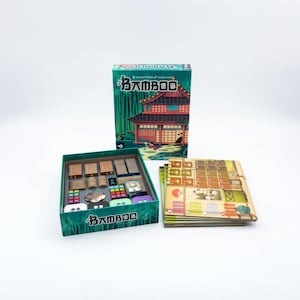 May include: A board game set with a green box and components. The box features a Japanese-style building illustration. Inside the box are wooden pieces, cards, and other game components. The game boards are stacked next to the box.