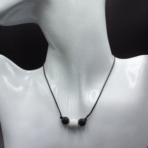 May include: A black cord necklace with three lava rock beads, two black and one white.
