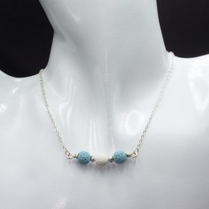 May include: A silver chain necklace with three lava rock beads. The beads are blue and white.