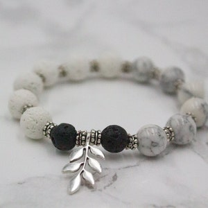 May include: A white and black beaded bracelet with a silver leaf charm. The bracelet is made with lava rock and white marble beads.