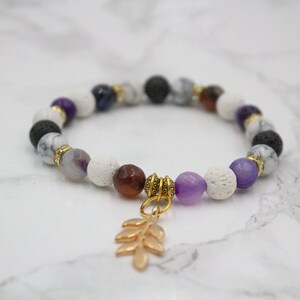 May include: A bracelet made with white, black, purple, and brown beads with a gold leaf charm.