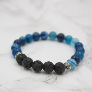 May include: A blue and black beaded bracelet with silver accents. The bracelet is made with blue agate and black lava rock beads.