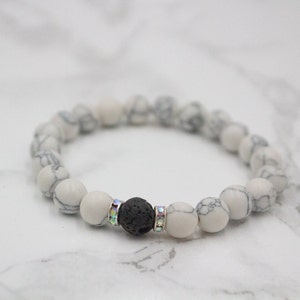 May include: White and gray beaded bracelet with a black lava stone bead and clear rhinestone accents.