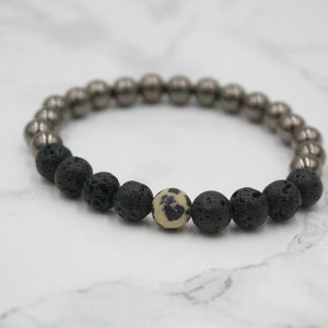 May include: A black lava rock and silver bead bracelet with a single white and black speckled bead.