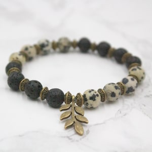 May include: A bracelet with black lava rock beads, speckled stone beads, and antique brass details. A decorative brass leaf charm is attached. The bracelet is designed for a comfortable fit. The beads are measured in centimetres.