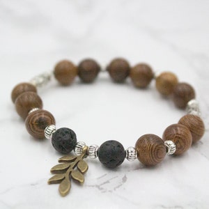 May include: A brown wood and black lava rock beaded bracelet with a silver metal accent and a bronze leaf charm.