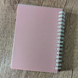 May include: A pink spiral bound notebook with a clear plastic cover.