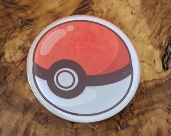 May include: A round button featuring a red and white design, reminiscent of a Pokeball. The button has a glossy finish and a brown border. The button is a collectible item.