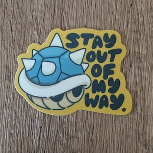 May include: A yellow sticker with a blue and white cartoon character of a spiked shell. The text "STAY OUT OF MY WAY." is written in black on the sticker.