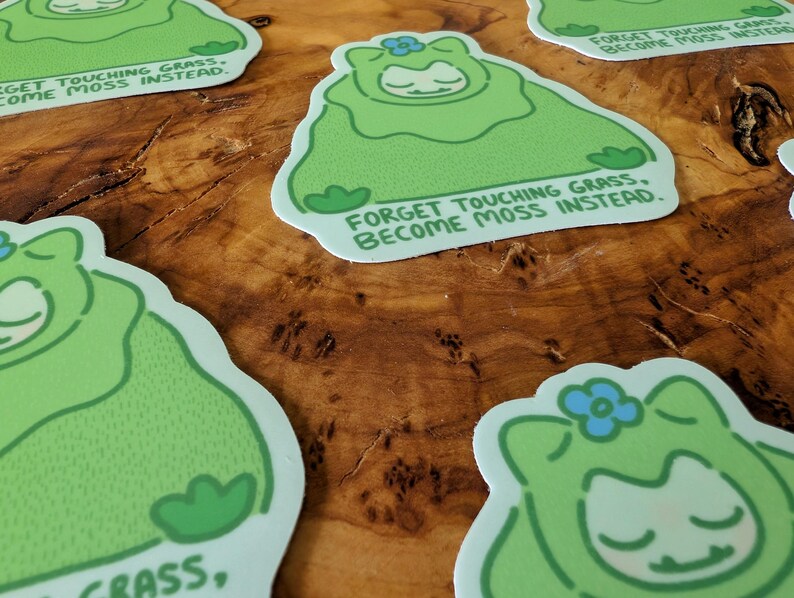 Peut inclure: Plusieurs autocollants repr&eacute;sentant un personnage de dessin anim&eacute; dans un costume de mousse vert avec une fleur bleue. Le texte dit : "Oubliez de toucher l'herbe, devenez de la mousse &agrave; la place."
