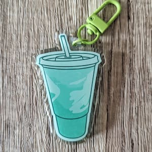 May include: A green and white plastic keychain shaped like a cup with a straw. The keychain has a green metal clasp.