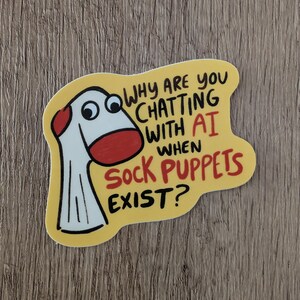 May include: A die-cut sticker with a yellow background featuring a white sock puppet with a red heel and toe. The text reads: WHY ARE YOU CHATTING WITH AI WHEN SOCK PUPPETS EXIST? The lettering is in black and red, with the sock puppet looking right.