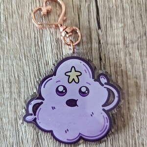 May include: A purple and glitter-filled keychain shaped like a cartoon cloud with a star on top and a surprised expression. The keychain has a rose gold metal clasp.