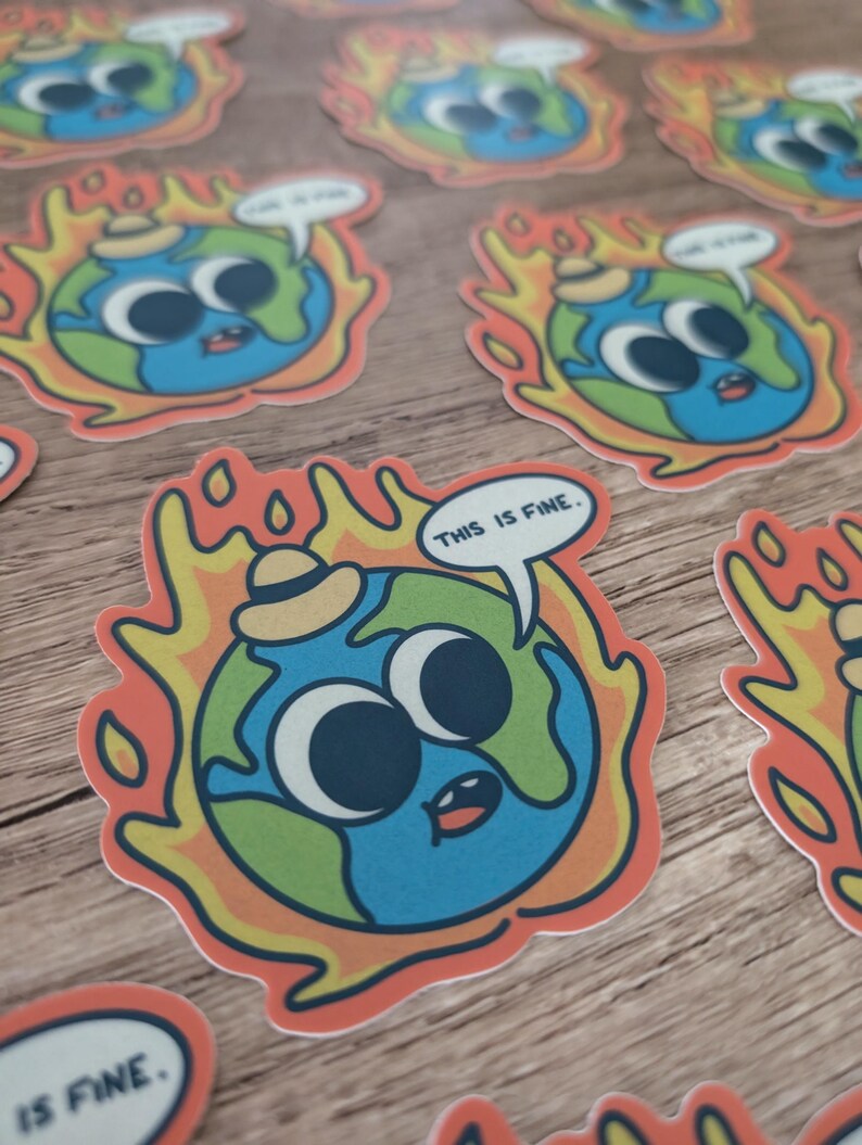 K&ouml;nnte beinhalten: Ein Aufkleber mit einer Cartoon-Erde, die einen Hut tr&auml;gt und in Flammen steht, mit dem Text "This is fine." in einer Sprechblase. Die Erde hat gro&szlig;e Augen und einen &uuml;berraschten Ausdruck.