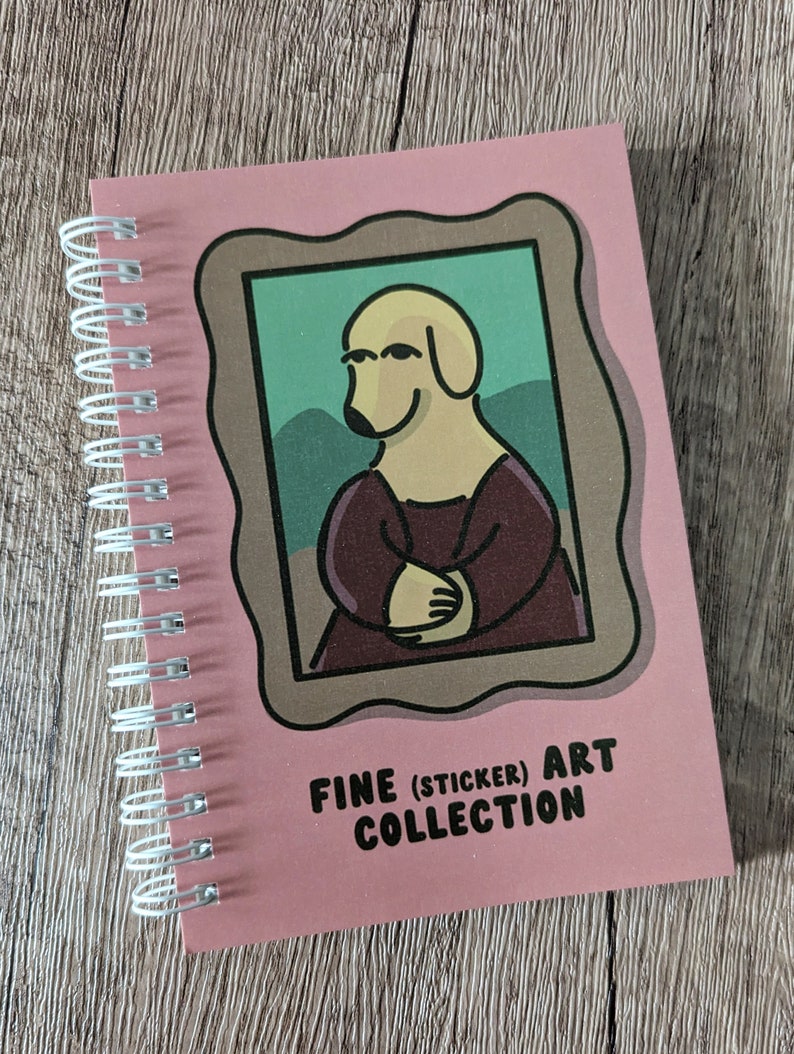 May include: A pink spiral bound notebook featuring a cartoon dog in a painting frame. The cover text reads "Fine (Sticker) Art Collection".
