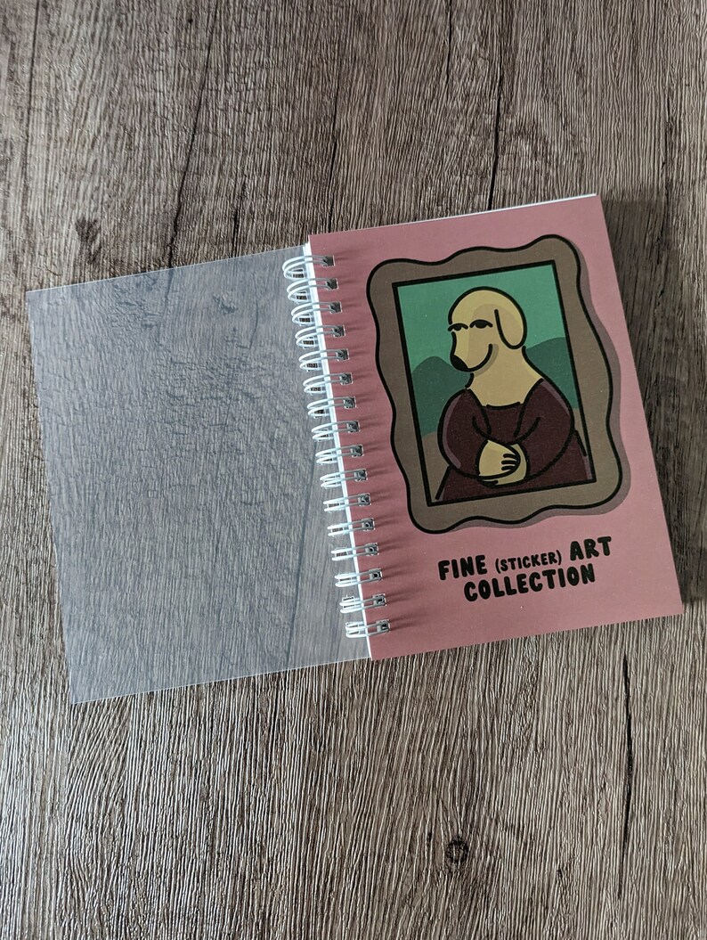 May include: A pink spiral bound notebook with a clear plastic cover. The front cover features a cartoon dog in a frame with the text "Fine (Sticker) Art Collection".