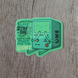 May include: A green sticker featuring the character BMO from Adventure Time. The sticker has the text "Sometimes life is scary + dark, that is why we must find the light." BMO is depicted with arms and legs, and a smiling face.