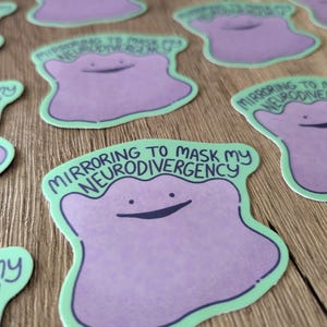 May include: A sticker with a purple cartoon character with a green outline. The character has a big smile and the text "Mirroring to mask my neurodivergency" is written in black above the character.