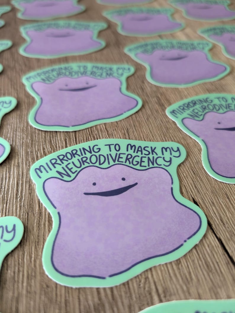 May include: A sticker with a purple cartoon character with a green outline. The character has a big smile and the text "Mirroring to mask my neurodivergency" is written in black above the character.