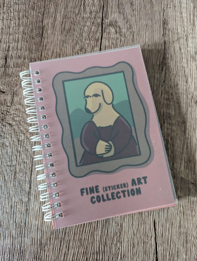 May include: A pink spiral bound notebook featuring a cartoon dog in a painting frame. The dog is wearing a purple dress and has a yellow body. The text on the cover reads "FINE (STICKER) ART COLLECTION".
