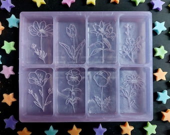 Könnte beinhalten: Eine transparente, violette Silikonform mit acht rechteckigen Vertiefungen. Jede Vertiefung hat ein anderes florales Design, das in den Boden geprägt ist. Die Form ist für die Herstellung von Seife, Kerzen oder Kunstharz-Gegenständen gedacht.