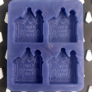 May include: A purple silicone mold with four cavities shaped like haunted houses. Each house has the words "Creepy Sweet Treat" inscribed on the front.
