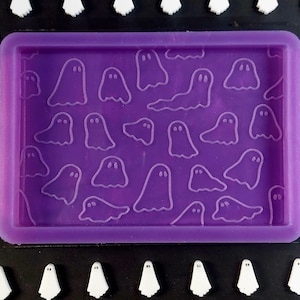 Peut inclure: Moule en silicone violet avec un motif de plusieurs fantômes blancs. Le moule est rectangulaire et possède un bord surélevé.
