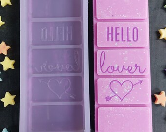 May include: A silicone mold for making wax melts with four sections. The mold is purple and has the words "Hello" and "lover" inscribed in the sections. A wax melt is shown in the mold, with the words "Hello" and "lover" and a heart with an arrow.