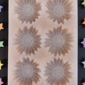 Può includere: Uno stampo in silicone con sei cavità a forma di girasole. Lo stampo è di colore marrone chiaro e ha una superficie liscia.