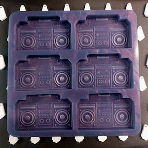 Pode incluir: Uma forma de silicone roxa com seis cavidades em forma de boomboxes vintage. A forma é projetada para fazer sabão, velas ou artesanato de resina.