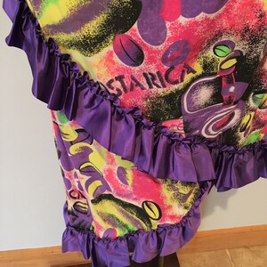 Pode incluir: Uma saia roxa e rosa com uma estampa abstrata colorida e as palavras "Costa Rica" na frente. A saia tem uma bainha de babados roxos.