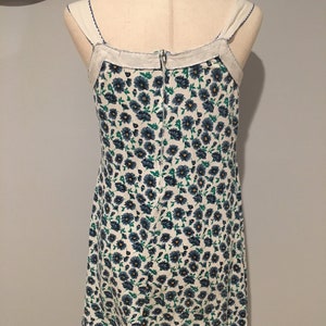 May include: A white sleeveless dress with a blue and green floral print. The dress has a zipper closure in the back and a white trim around the neckline.