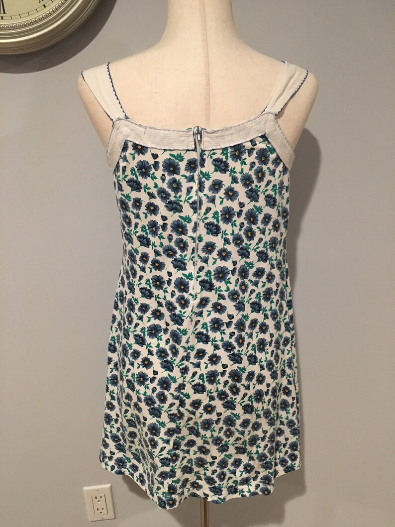 May include: A white sleeveless dress with a blue and green floral print. The dress has a zipper closure in the back and a white trim around the neckline.