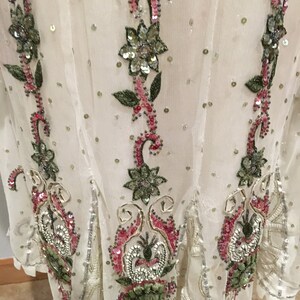 May include: A white sheer top with floral embroidery and sequins. The embroidery features pink, green, and silver sequins.