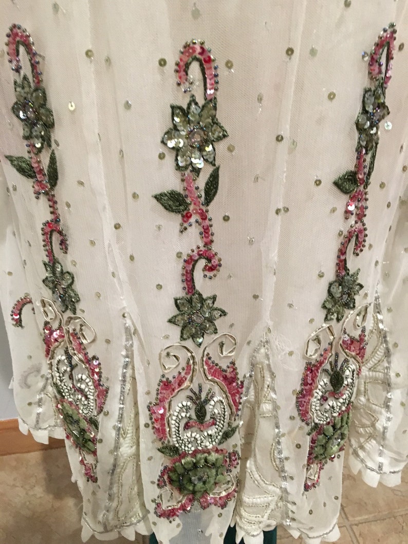 May include: A white sheer top with floral embroidery and sequins. The embroidery features pink, green, and silver sequins.