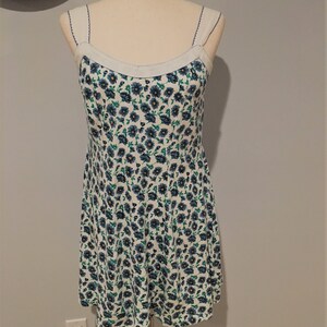 May include: A white sleeveless dress with a blue and green floral print. The dress has a scoop neck and thin straps.