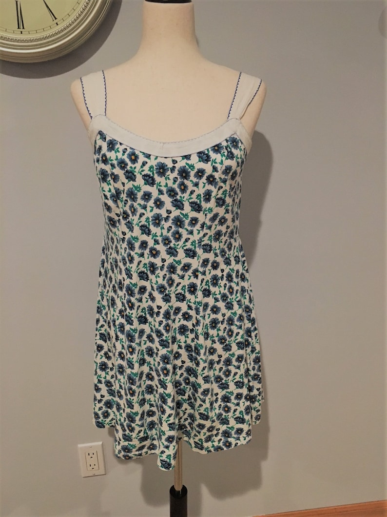 May include: A white sleeveless dress with a blue and green floral print. The dress has a scoop neck and thin straps.