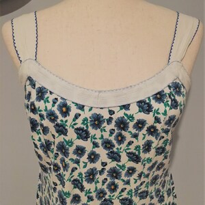 May include: A white sleeveless dress with a blue and green floral print. The dress has a white trim around the neckline and straps.