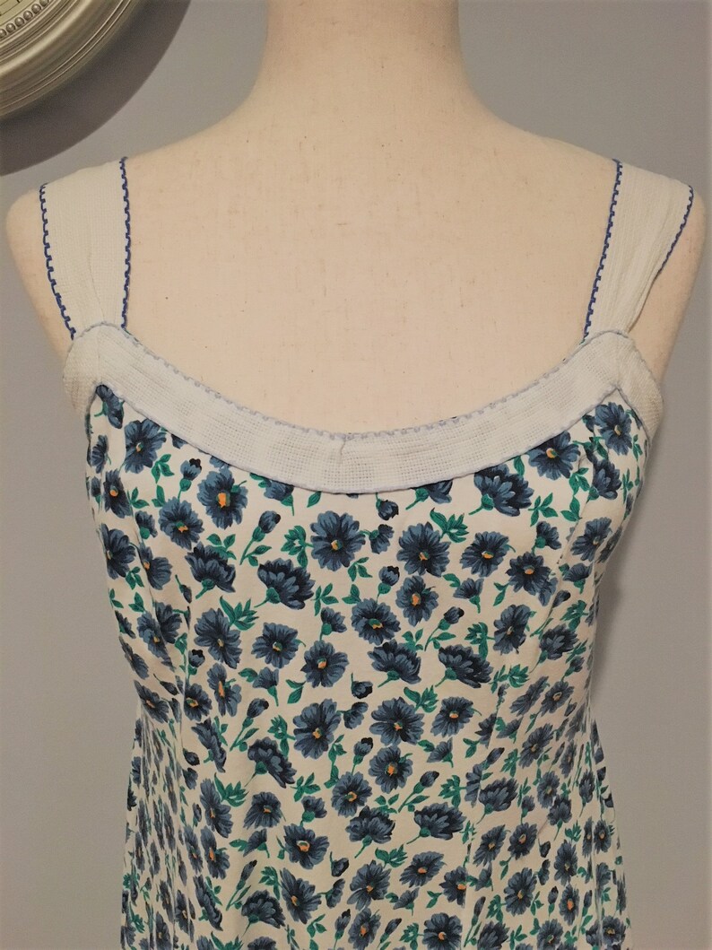 May include: A white sleeveless dress with a blue and green floral print. The dress has a white trim around the neckline and straps.