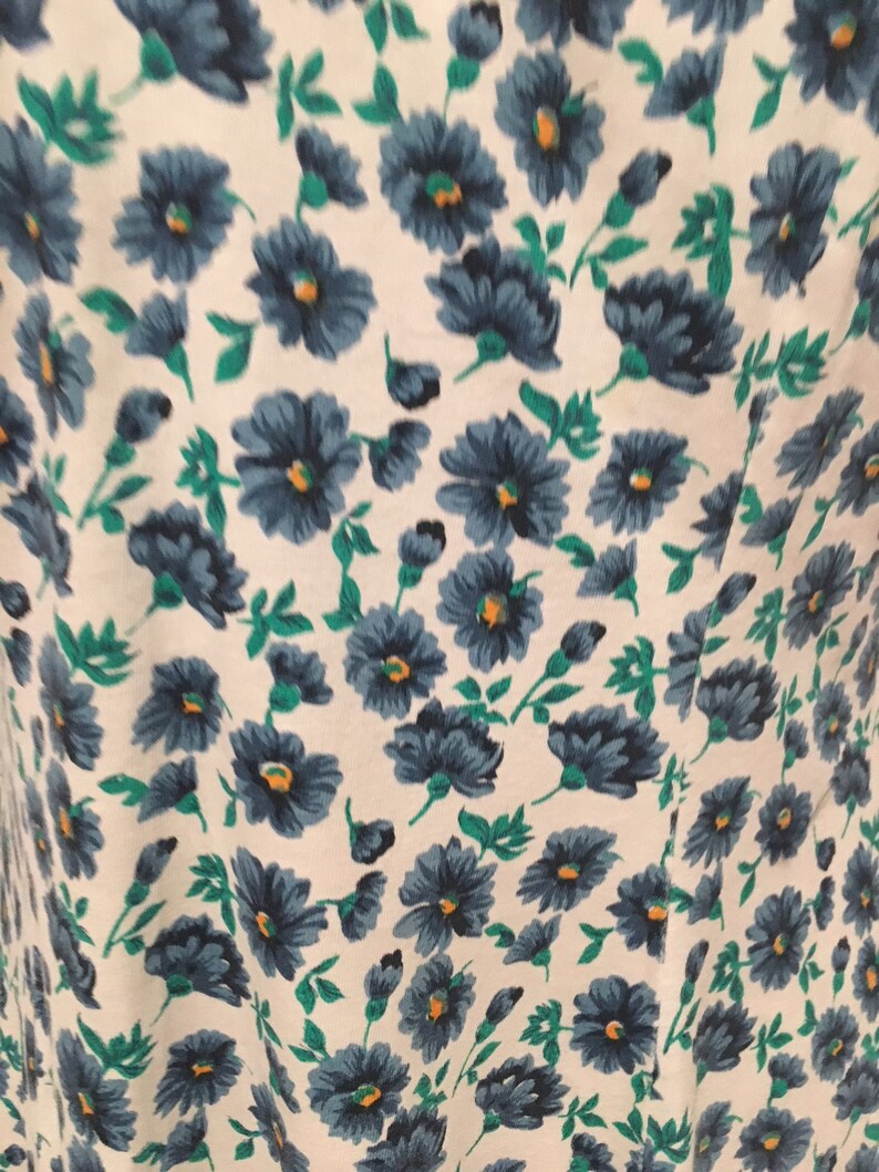 May include: White fabric with a blue and green floral pattern. The flowers are small and have a simple design.