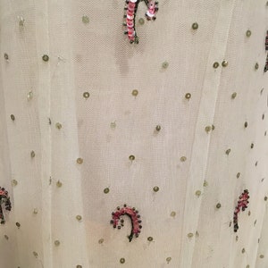 May include: White sheer fabric with a repeating pattern of small green sequins and larger pink and green sequins in a curved shape.