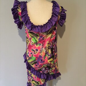 Pode incluir: Um vestido roxo e branco com estampa floral e o texto "Costa Rica" na frente. O vestido tem um decote e uma bainha com babados.